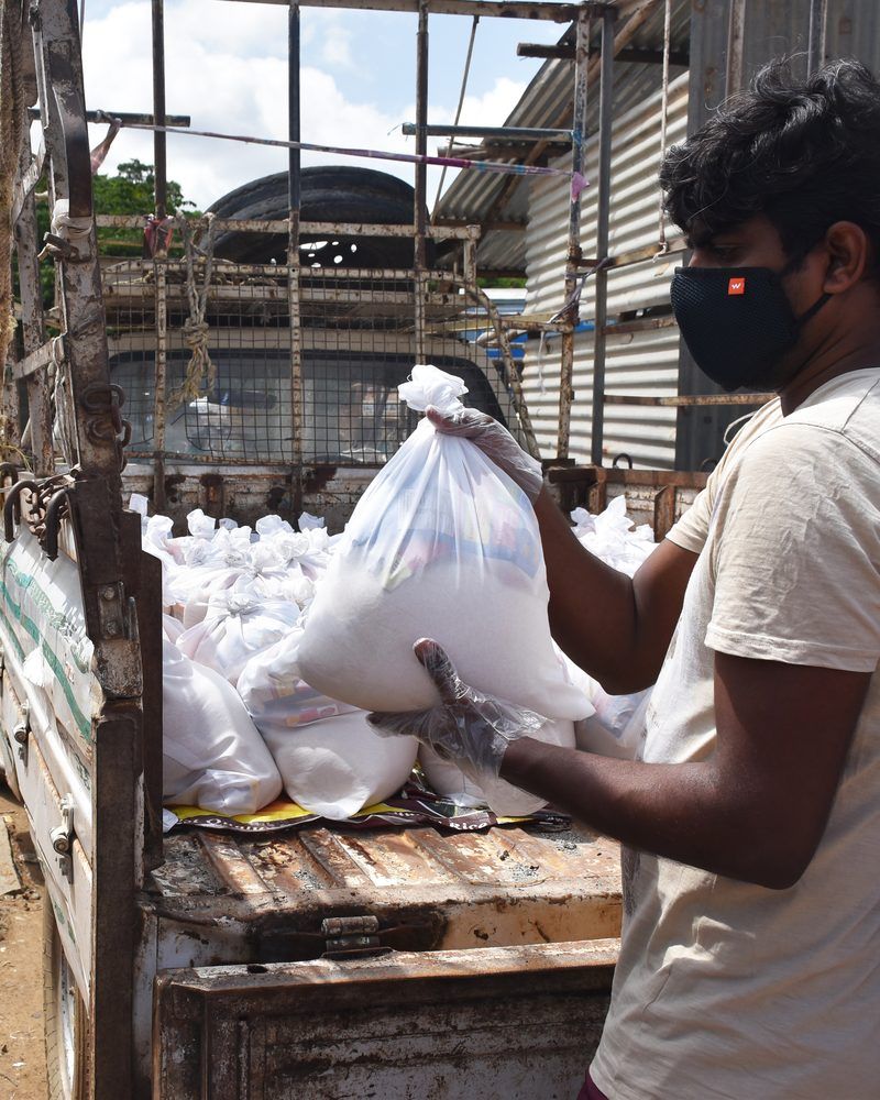A masked volunteer in gloves lifting a grocery kit off the back of a truck
