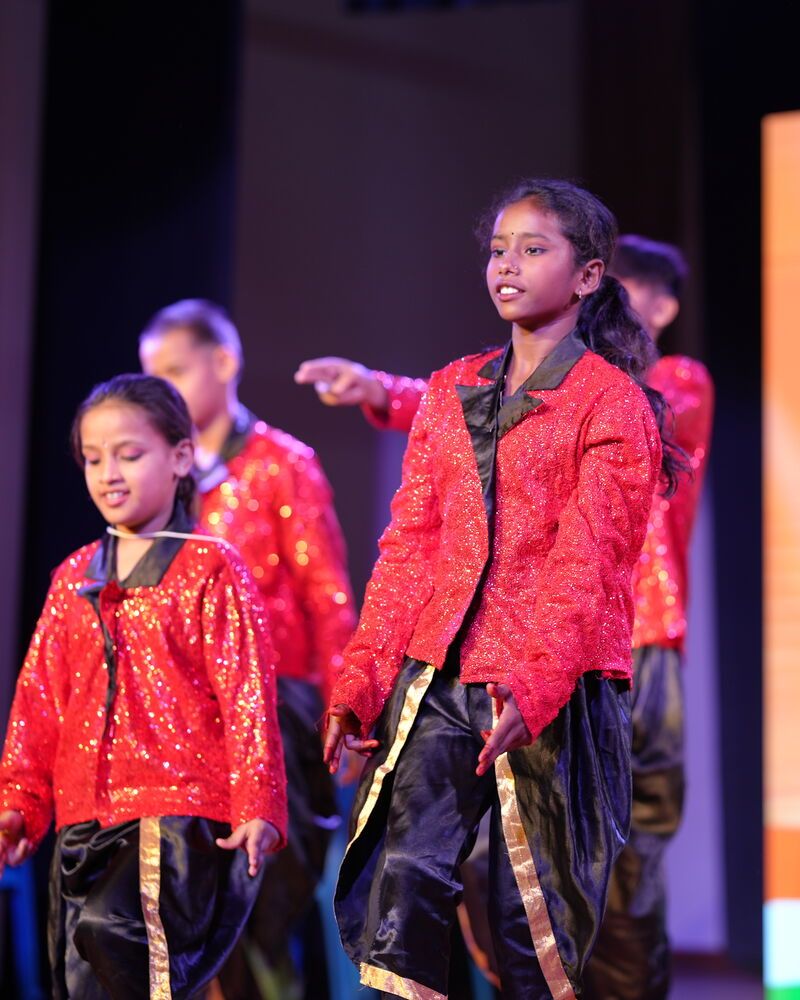 Children in red sequinned jackets dancing together on stage