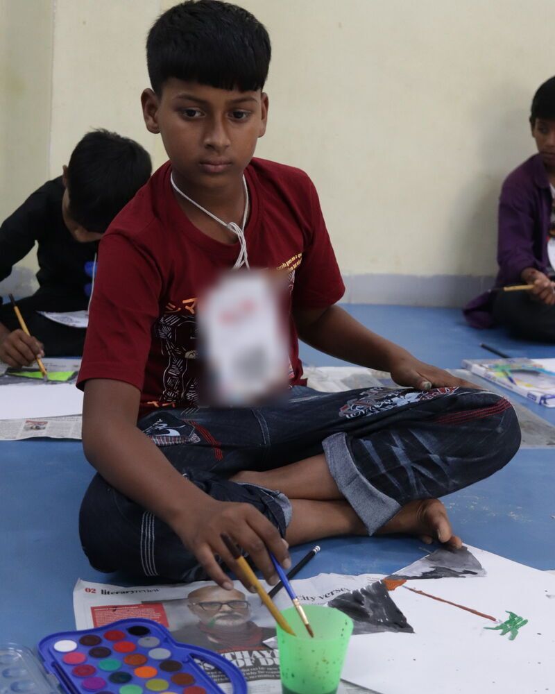 A boy sitting on the floor with a watercolour set and his painting