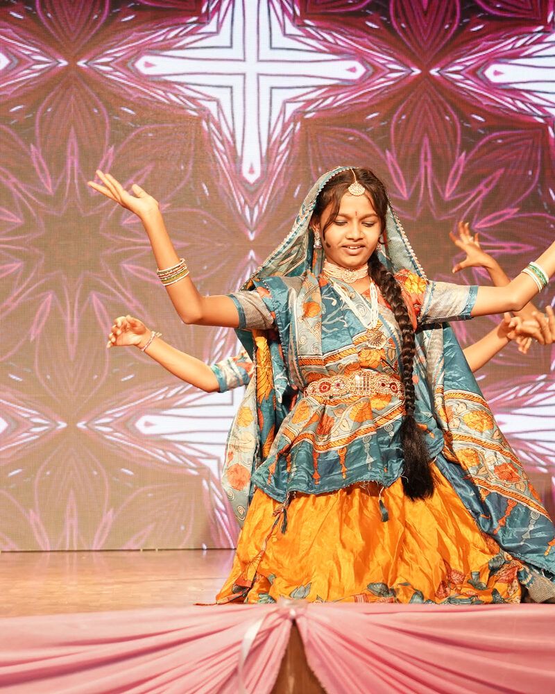 A girl in a mirror-work lehenga and dupatta dancing a folk dance on stage