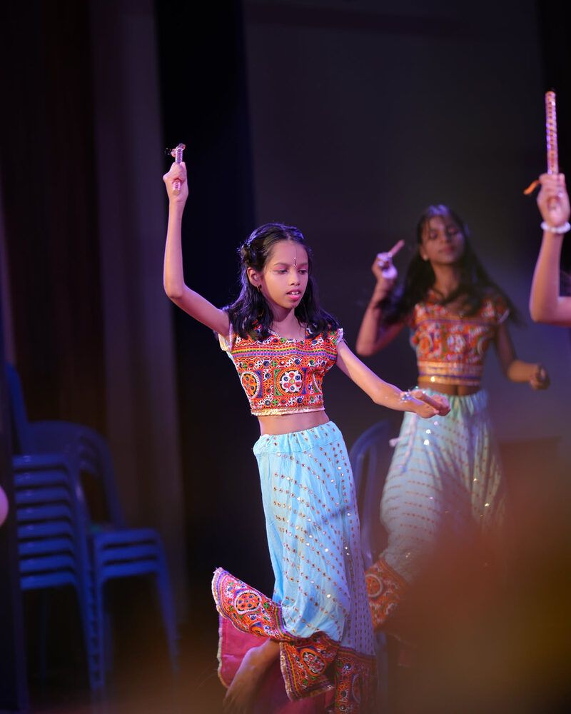 A girl in an embroidered blouse dancing with dandiya sticks raised