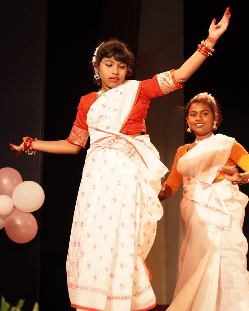 Two girls in white and red saris dancing a duet on stage