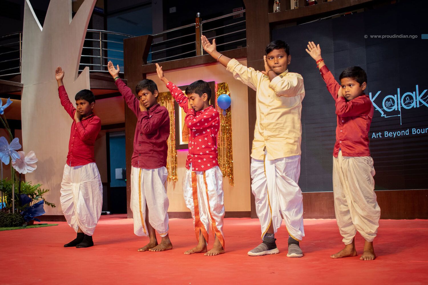 Five boys in kurtas and dhotis dancing in front of the Kalakriti banner at the first edition