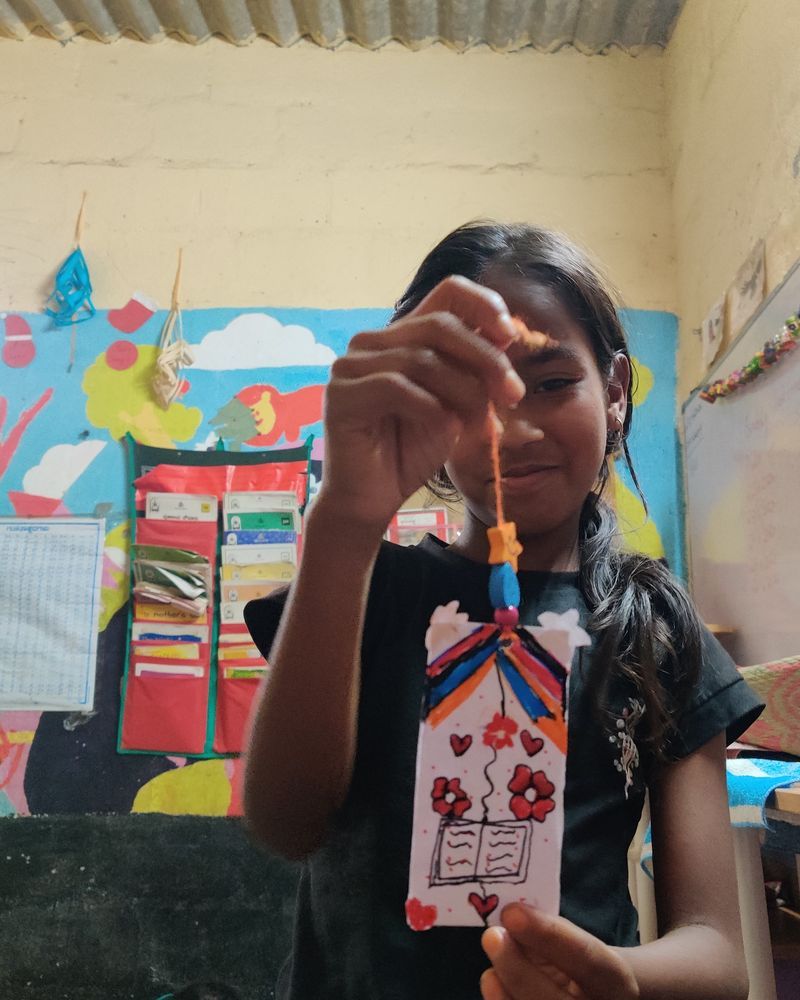 A girl holding up the bookmark she made in art and craft class