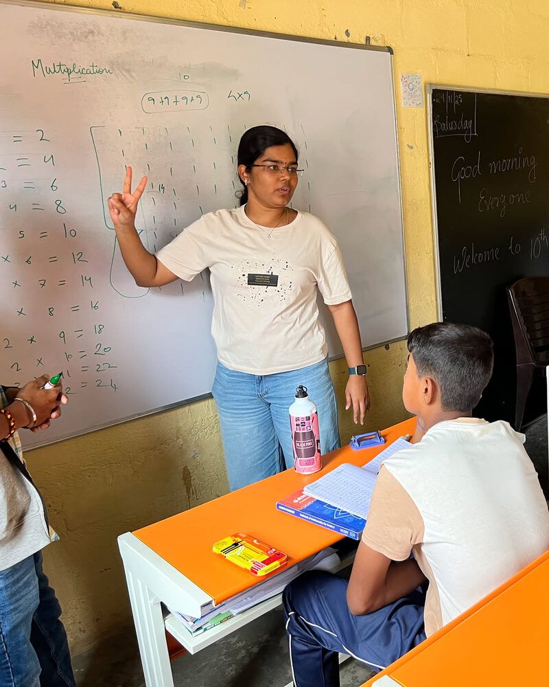 A volunteer at the whiteboard teaching multiplication to children at their desks